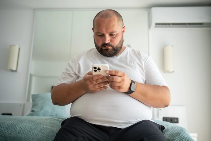 Homem sentado na cama consultando o celular
